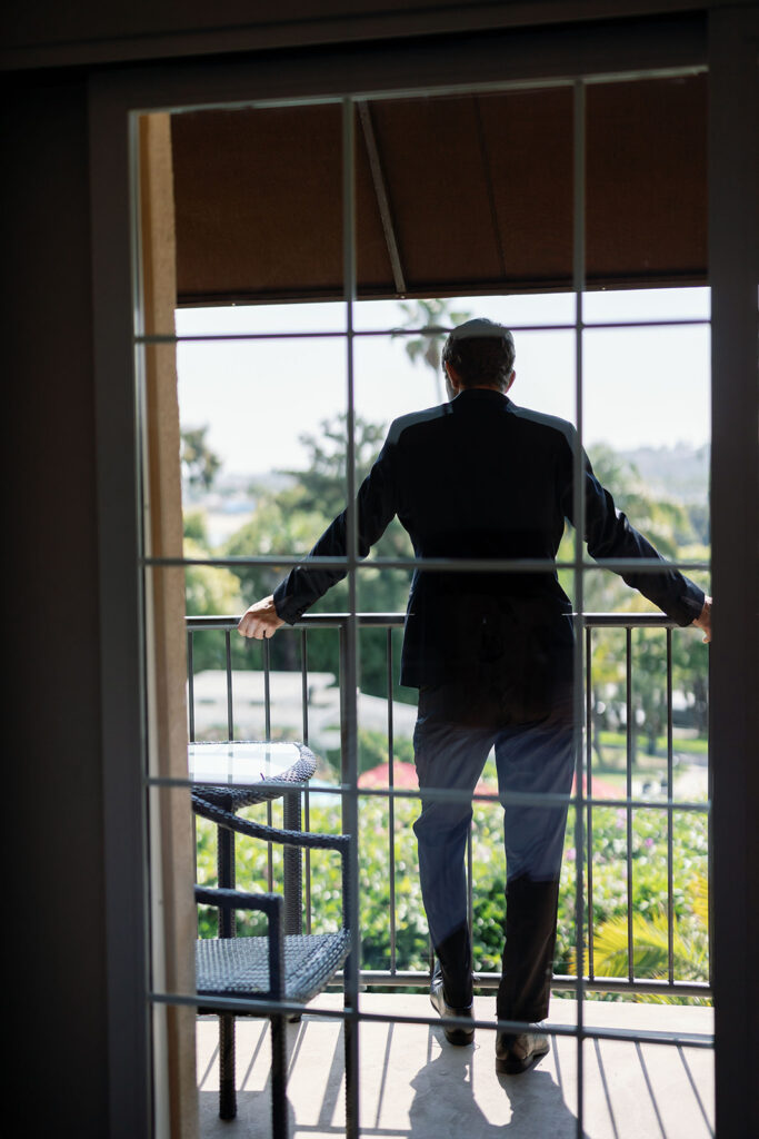 Groom standing on a hotel room balcony overlooking the grounds at Hyatt Regency Newport Beach.