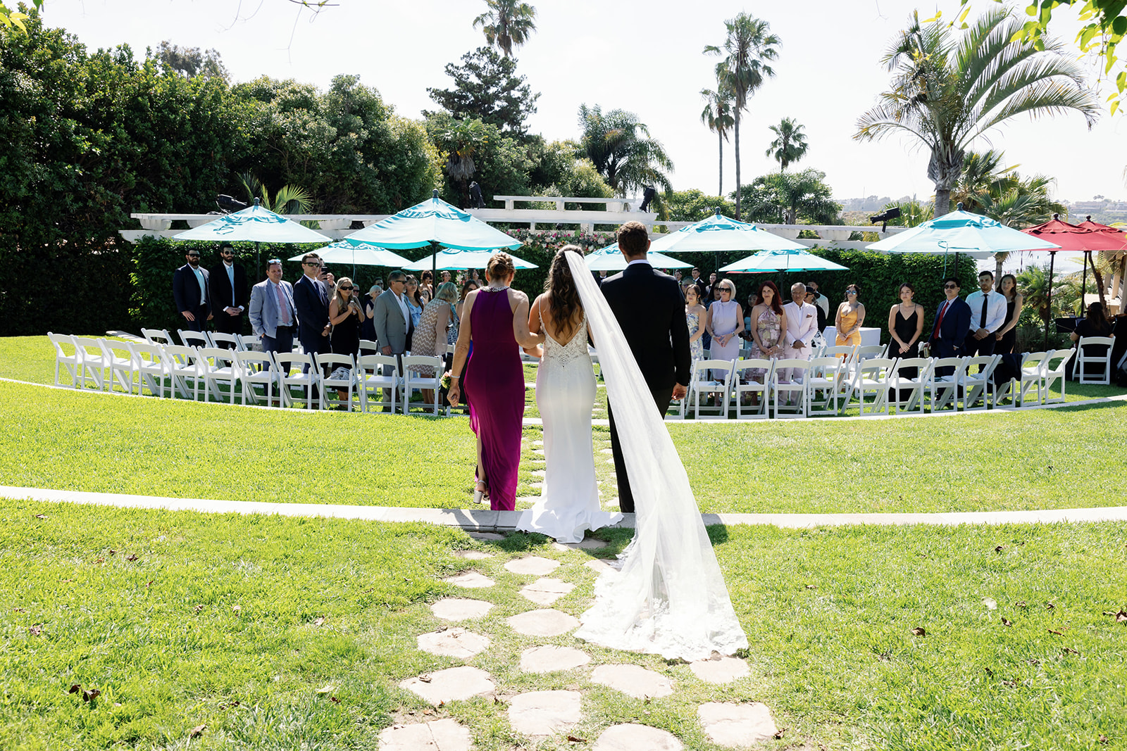 Bride walking down a stone pathway toward the outdoor Amphitheater ceremony with her veil trailing behind her.