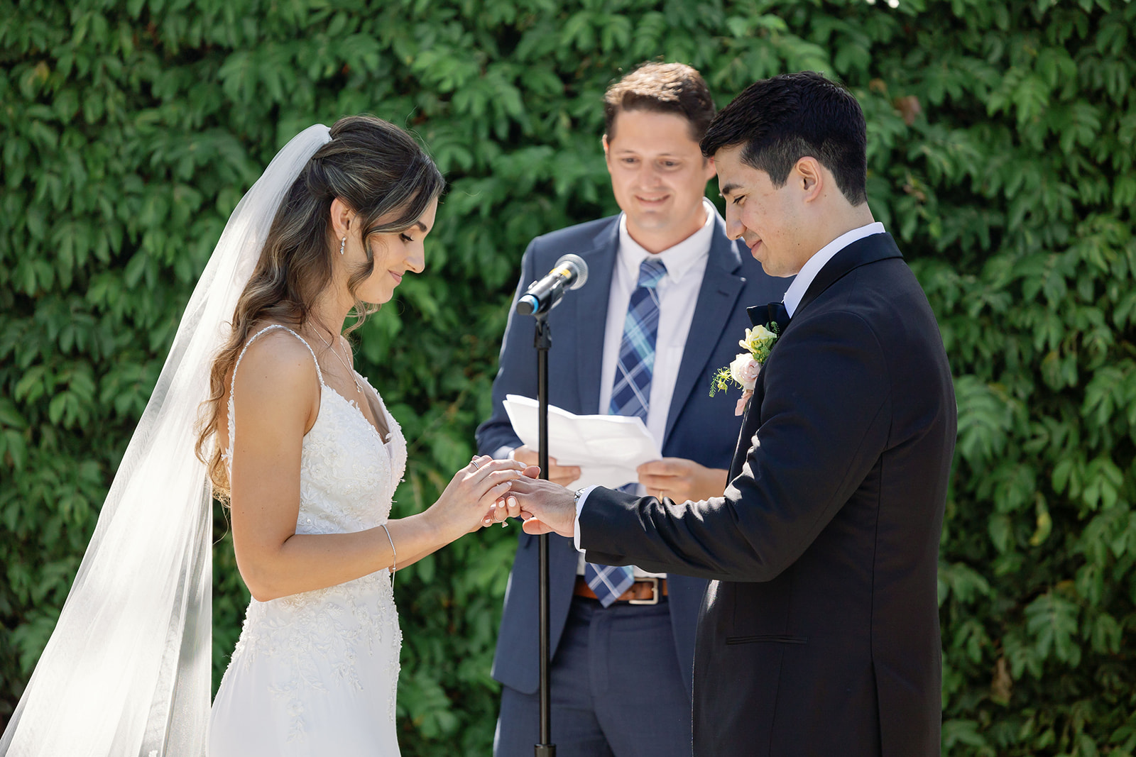 Bride placing a wedding ring on the groom’s hand during their outdoor ceremony.