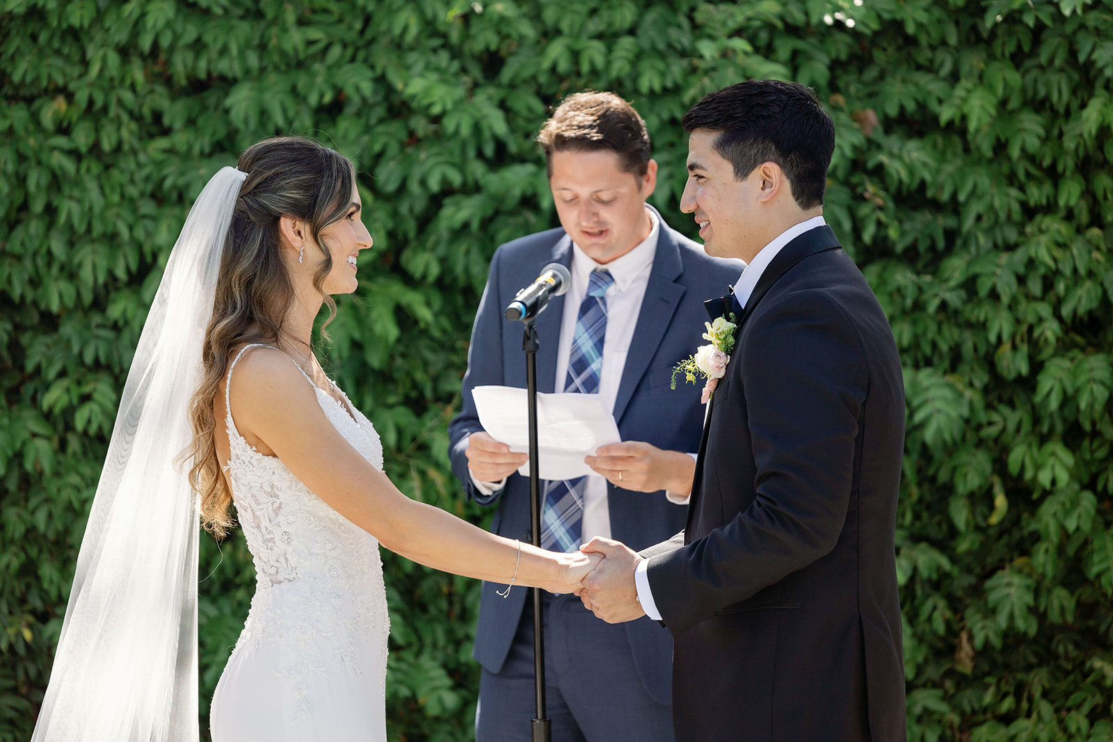 Couple holding hands while exchanging vows in front of lush greenery at the Hyatt Regency Newport Beach Amphitheater.