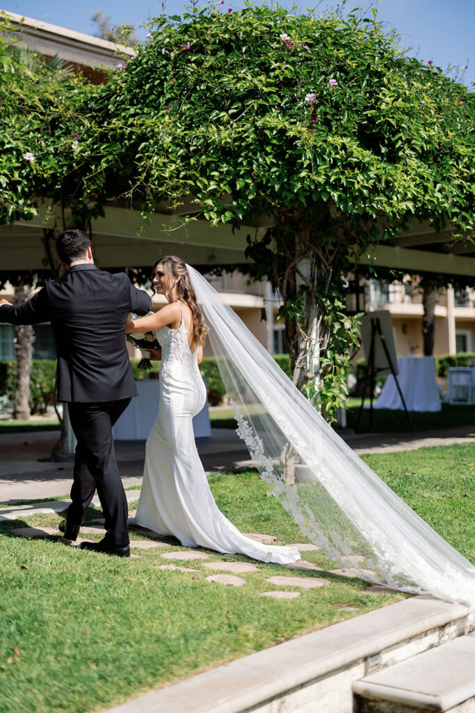 Couple walking beneath a vine-covered pergola after their Hyatt Regency Newport Beach Amphitheater ceremony.