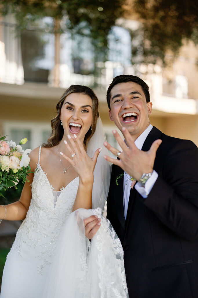 Newly married couple laughing and showing their wedding rings after the ceremony.