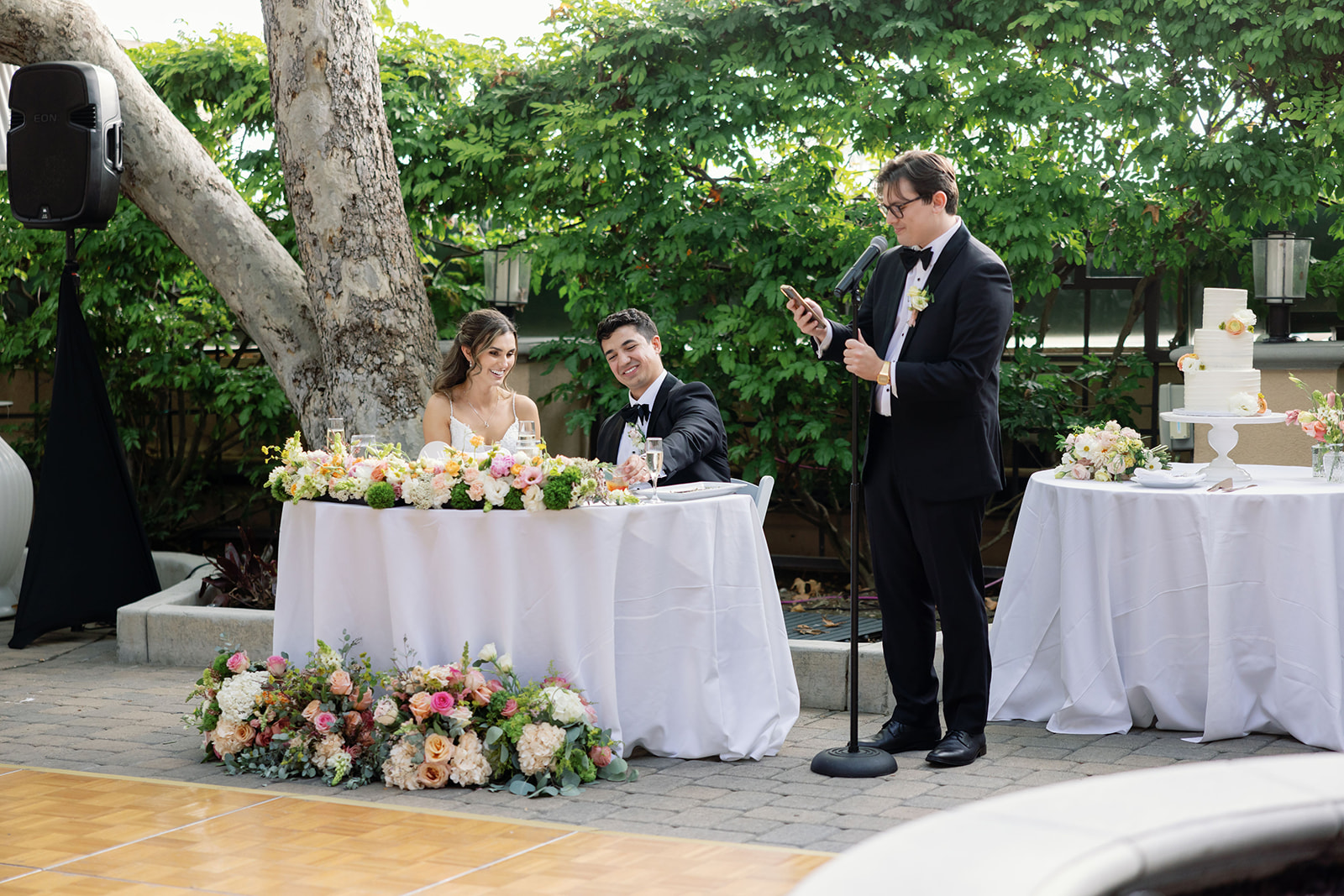 Wedding party member giving a toast beside the couple’s floral sweetheart table.