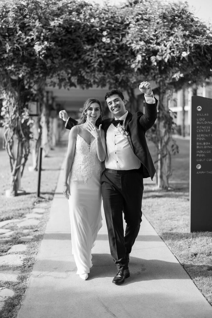 Newly married couple celebrating beneath a vine-covered pergola after their outdoor ceremony.