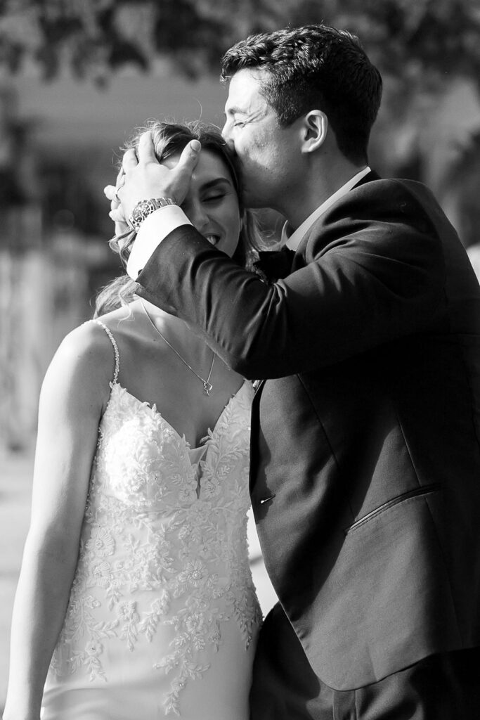 Groom kissing the bride’s forehead during black-and-white newlywed portraits.