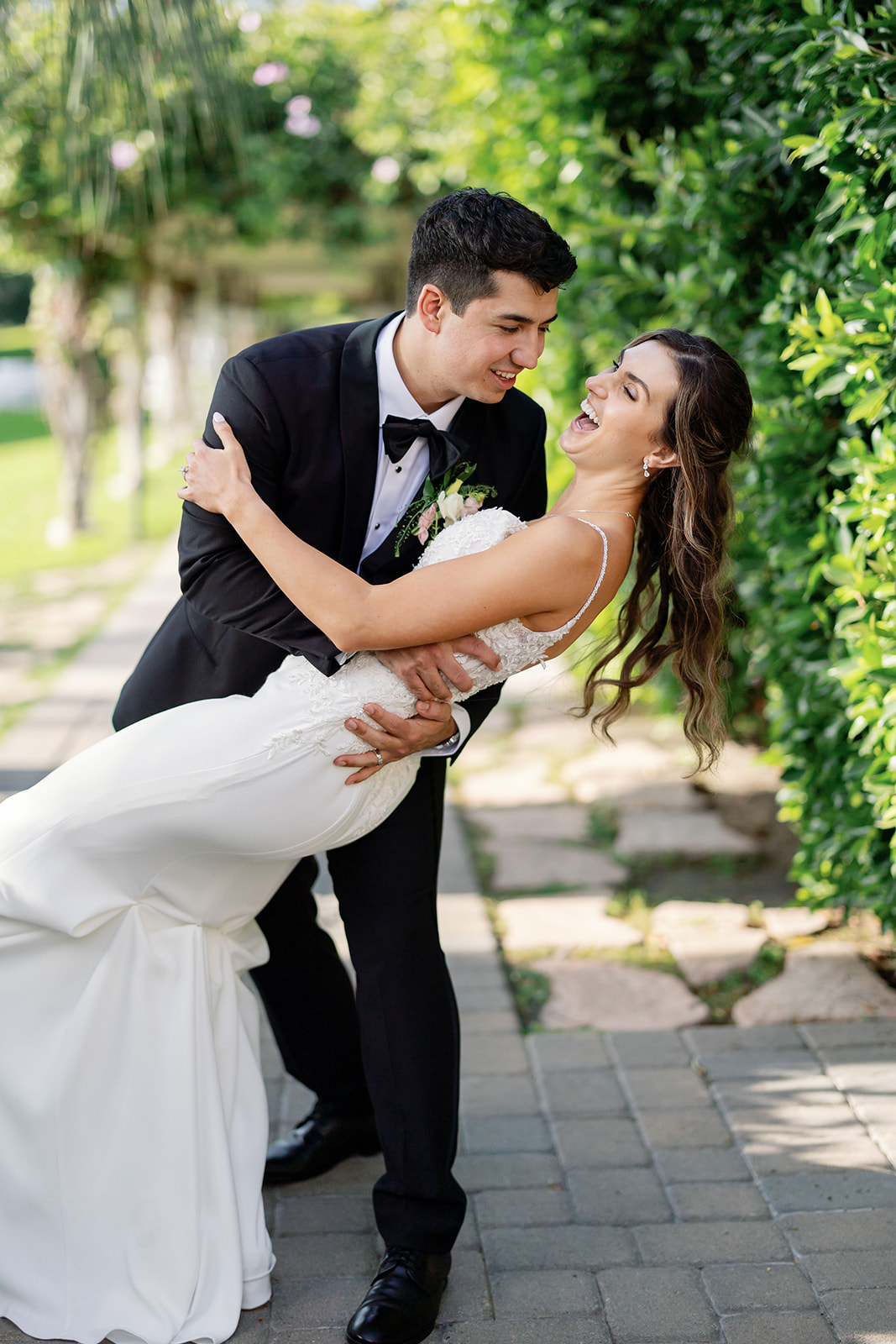 Groom dipping the bride during playful wedding portraits surrounded by greenery.
