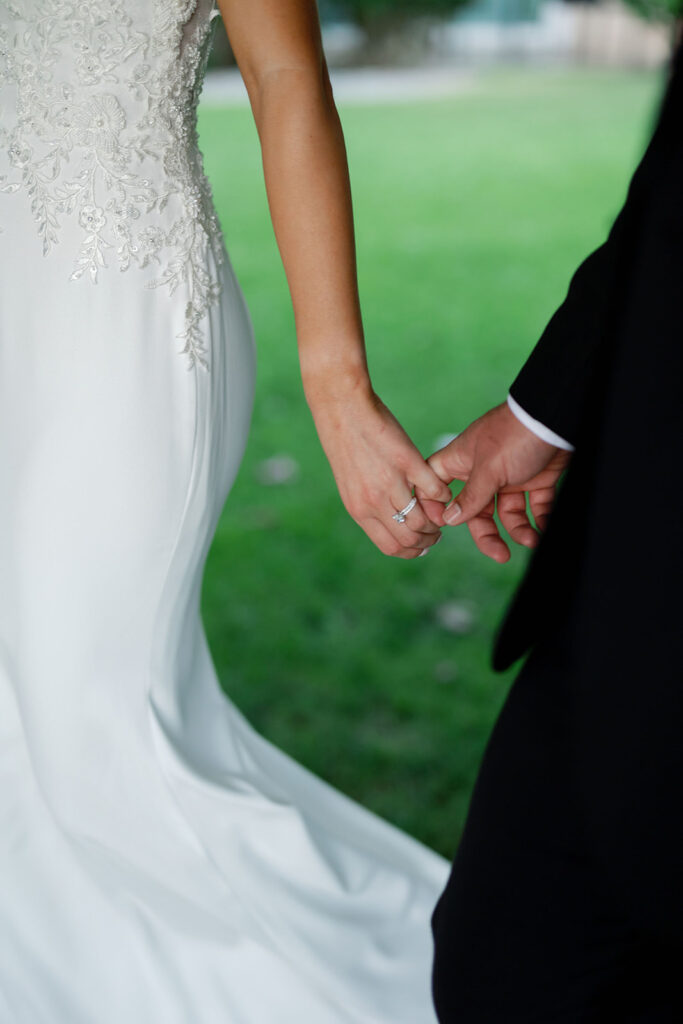 Close up shot of a bride and groom holding fingers as they walk together.