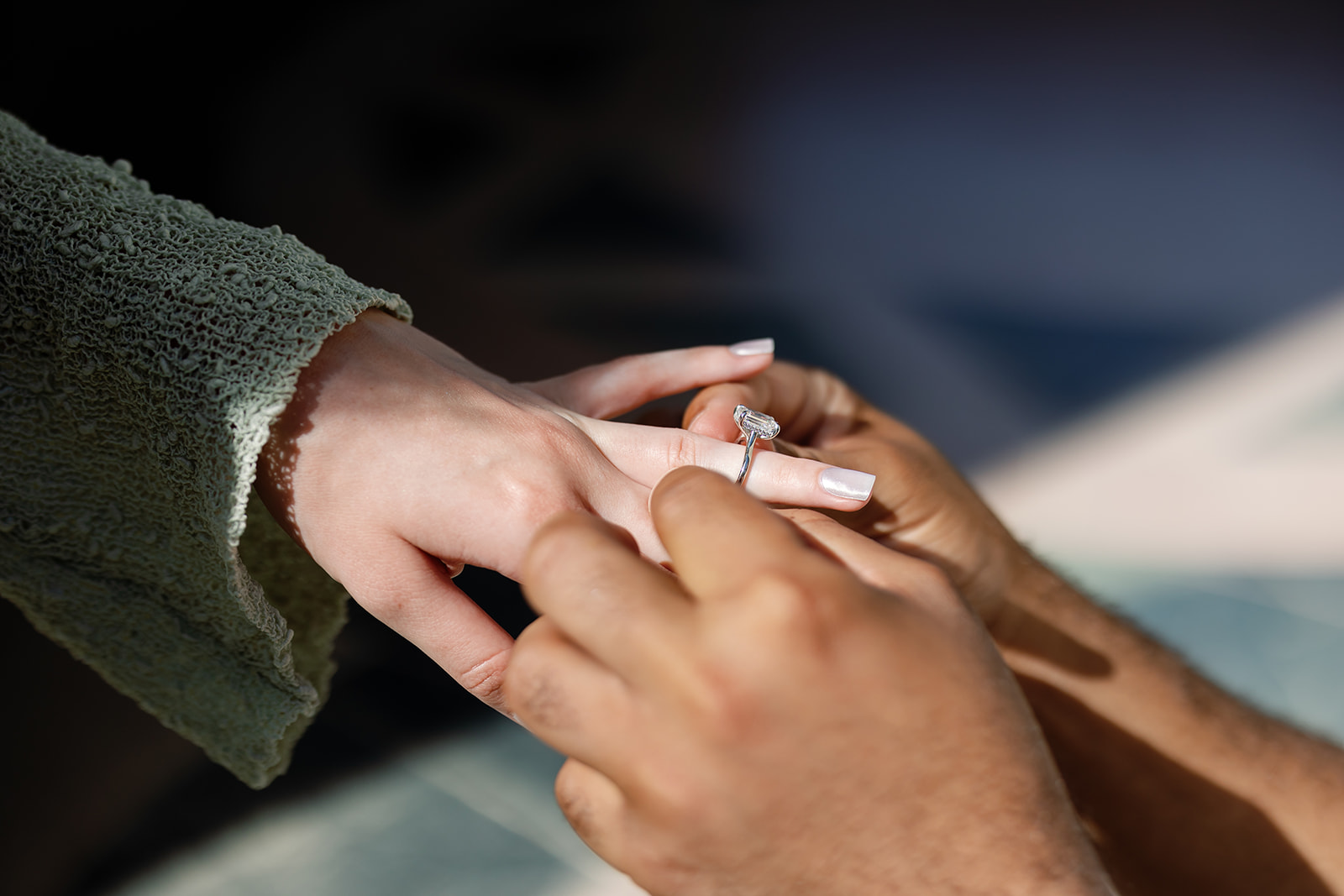 Close up shot of a man putting a ring on his fiancés finger during their proposal. 
