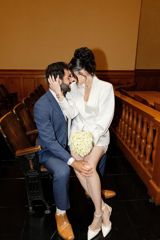 Bride and groom sitting in a wooden chair together during their Old Orange County Courthouse wedding in the Historic Room.