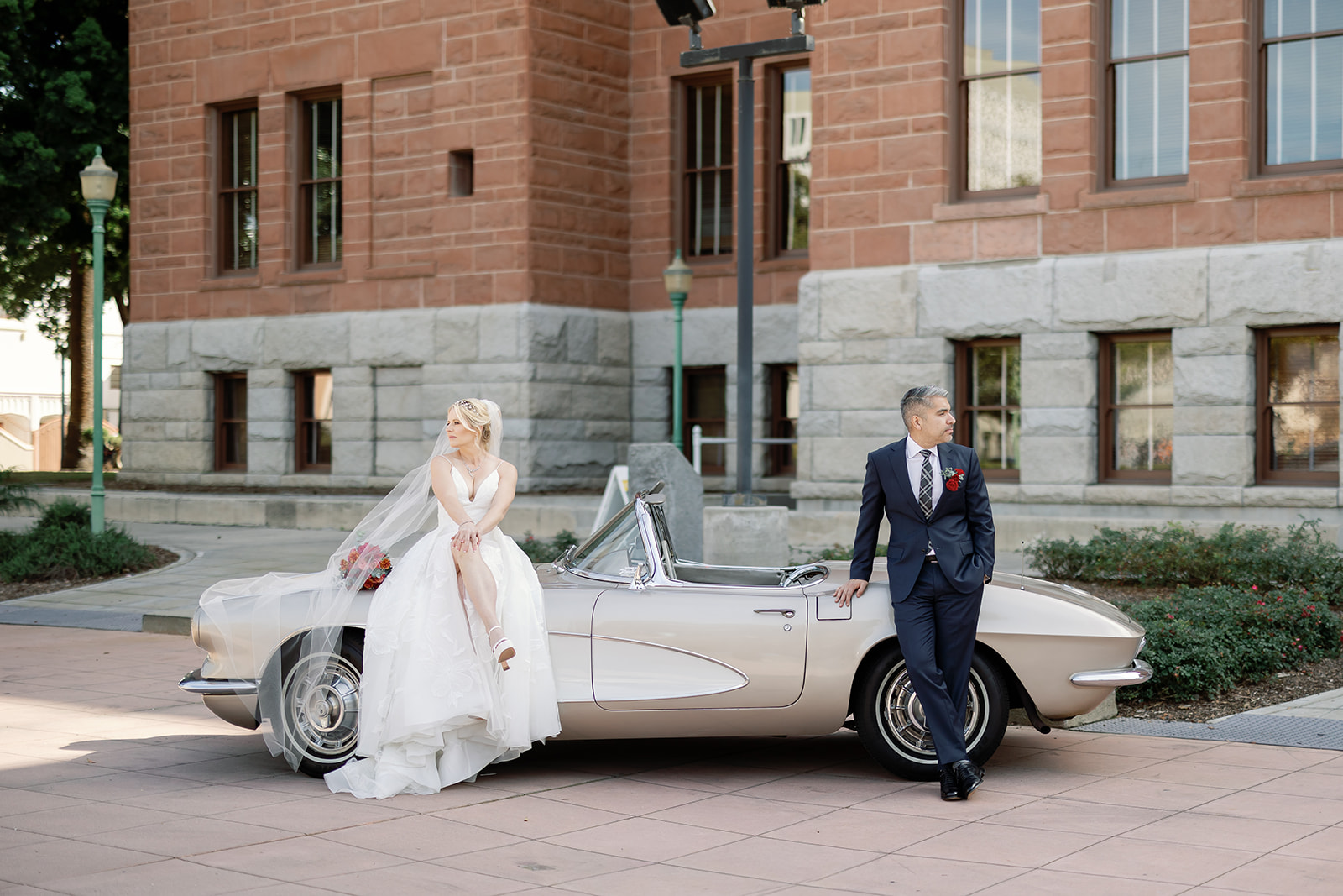 Bride and groom posing with a classic car in front the Old Orange County Courthouse in Santa Ana, California.