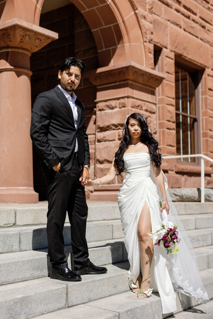 Bride and groom holding hands outdoors on the stairs for their Old Orange County Courthouse wedding in Santa Ana, California.