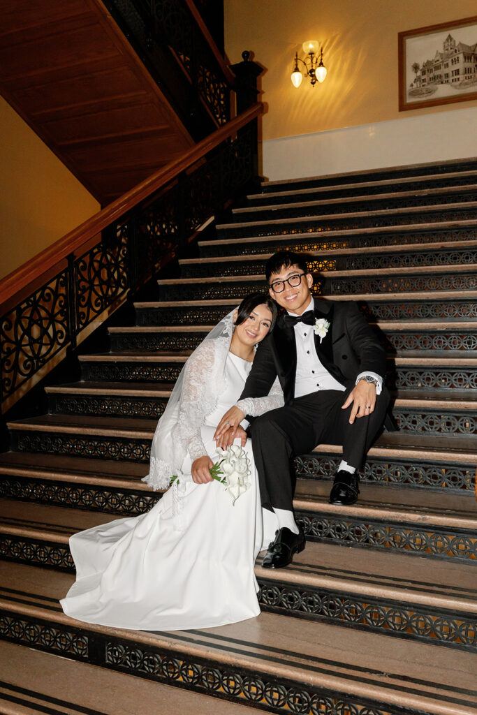 Bride and groom sitting on the indoor staircase inside The Old Orange County Courthouse in Santa Ana, California.