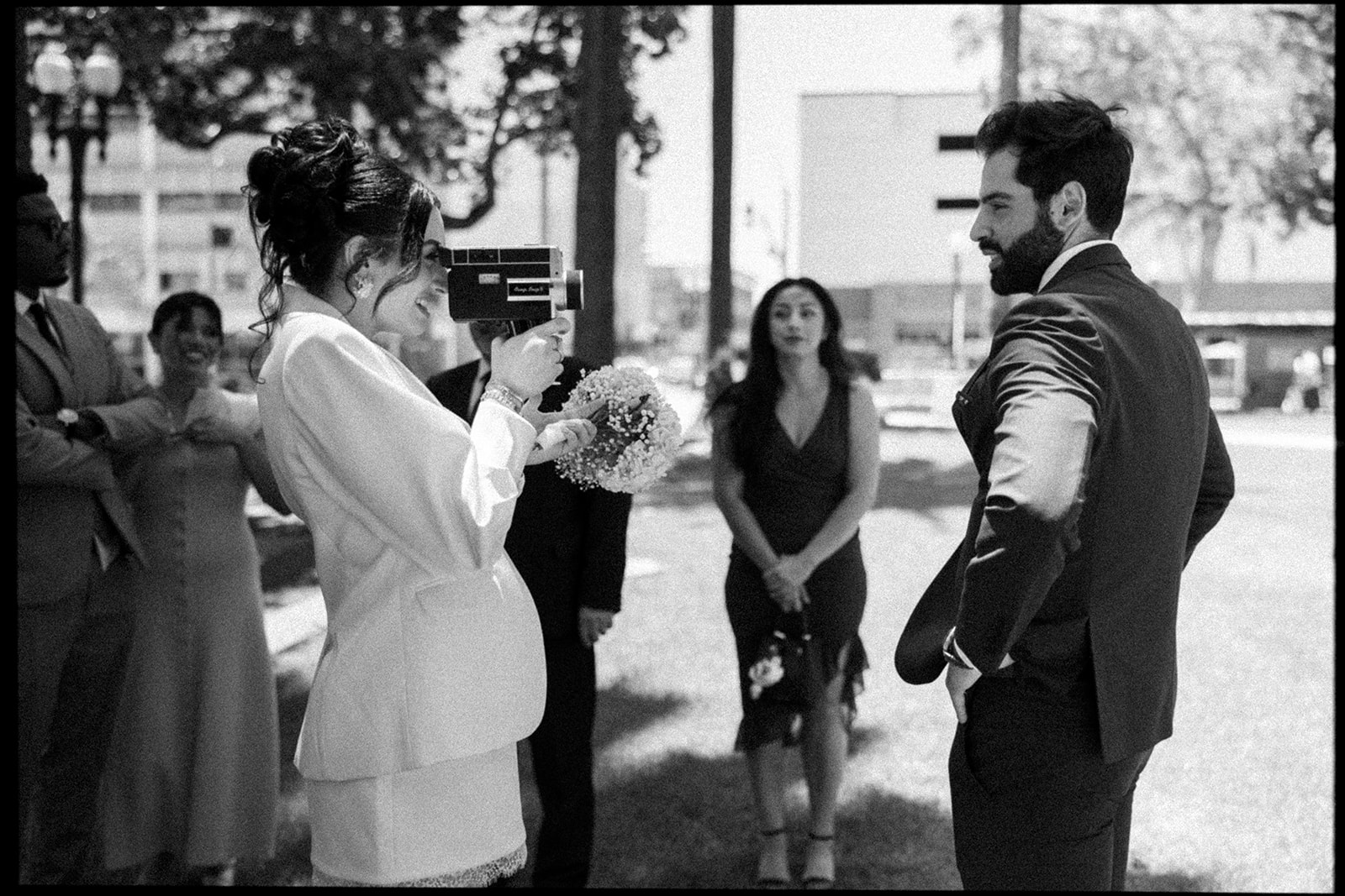 Black and white photo of a bride taking vintage video of the groom after their courthouse wedding.