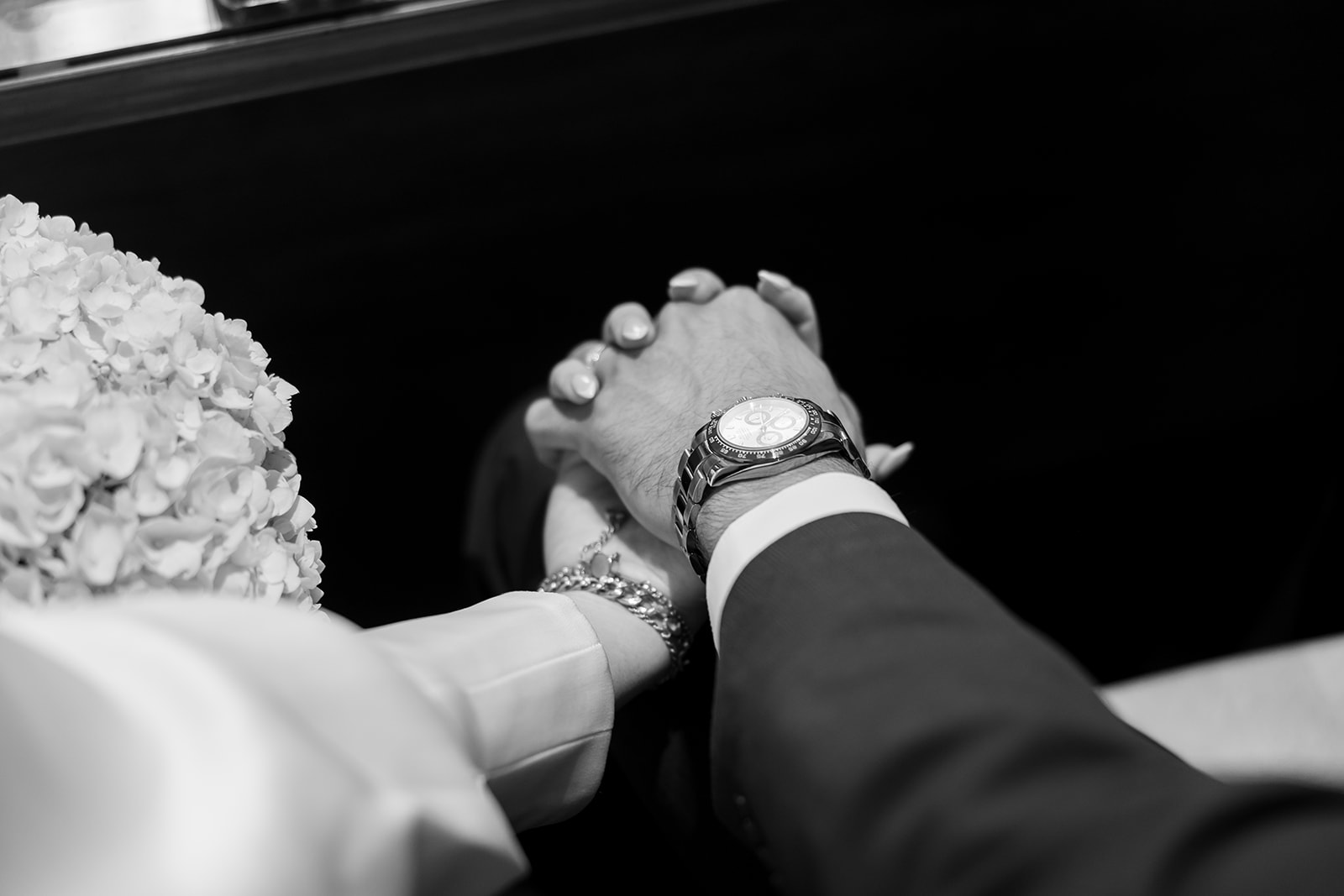 Black and white close up shot of a bride and groom holding hands during check in.